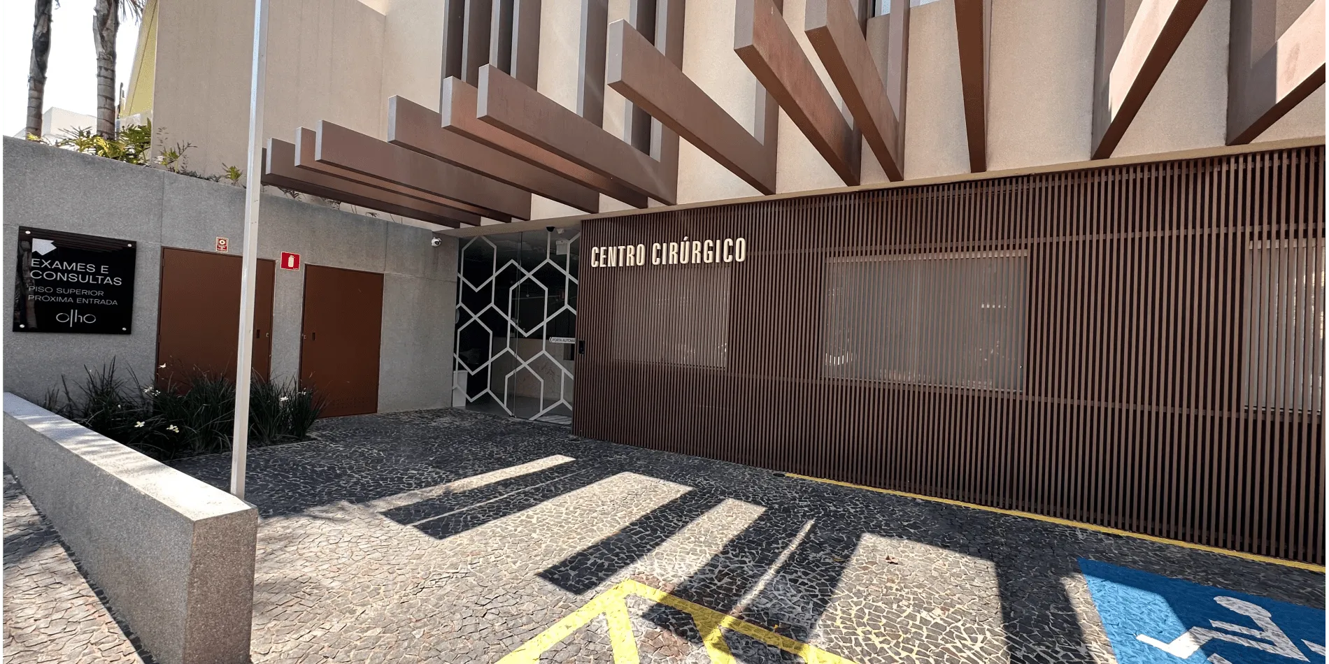Entrada do centro cirúrgico da Olho Clínica: fachada com ripado de madeira, letreiro "CENTRO CIRÚRGICO" e placa indicando exames e consultas no piso superior