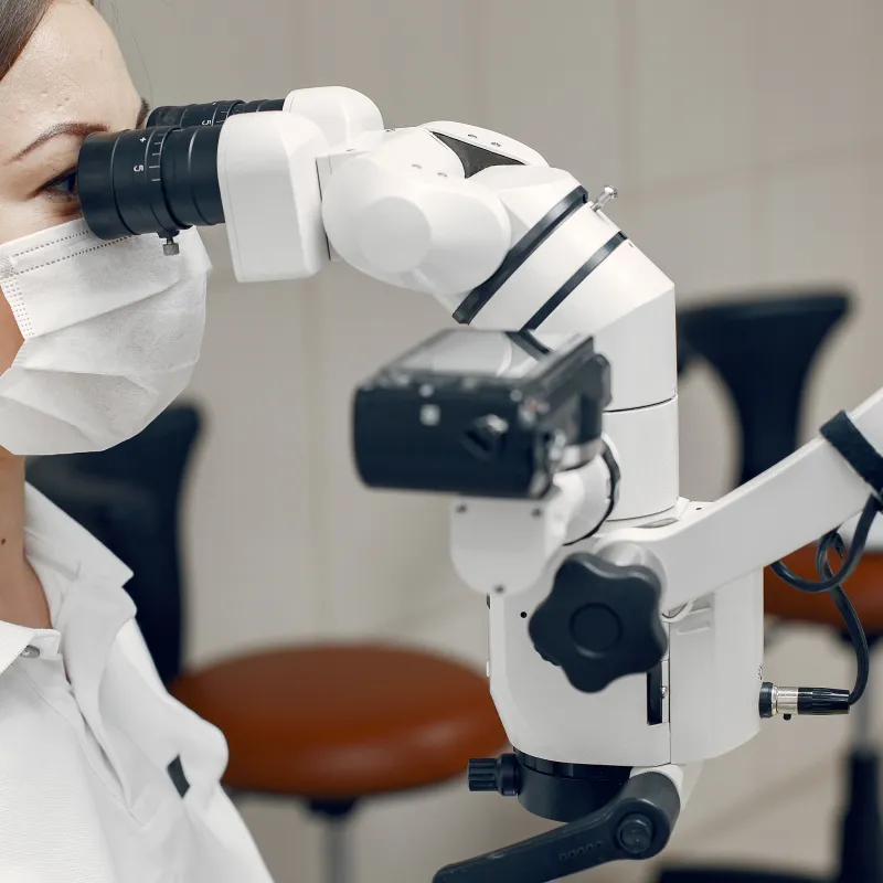 Oftalmologista de máscara e jaleco branco observando por um microscópio cirúrgico